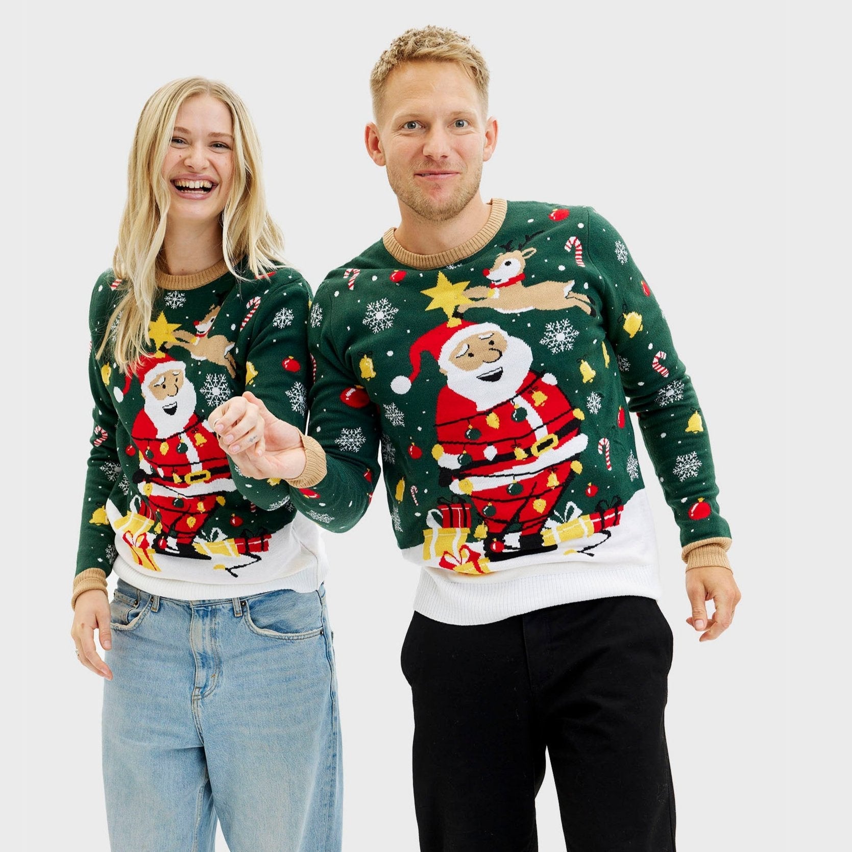 Een man met zijn handen langs zijn zij die een groene kersttrui met kerstman en lichtjes draagt.