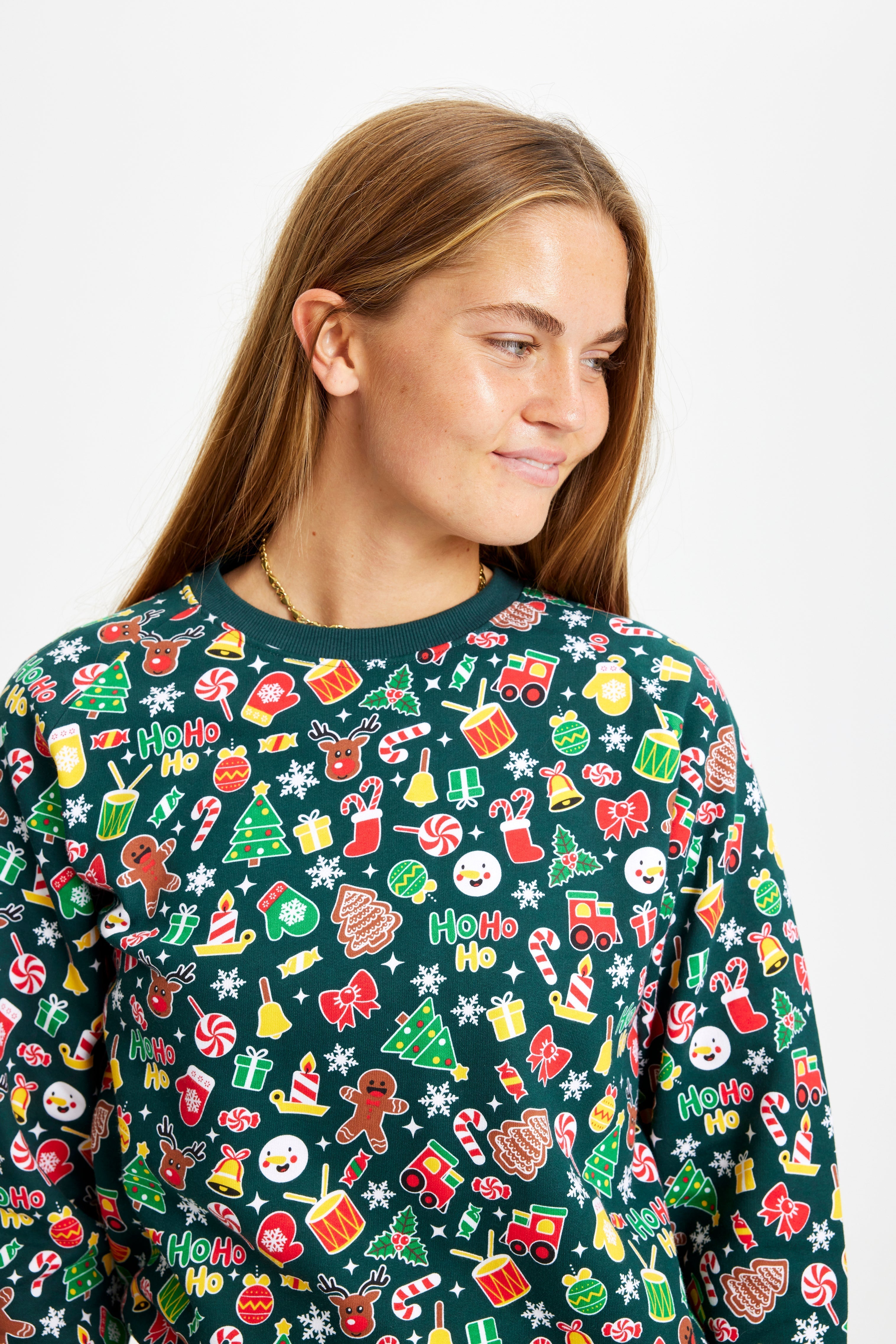 Een vrouw die opzij kijkt en een groene kersttrui met een kerstpatroon draagt.