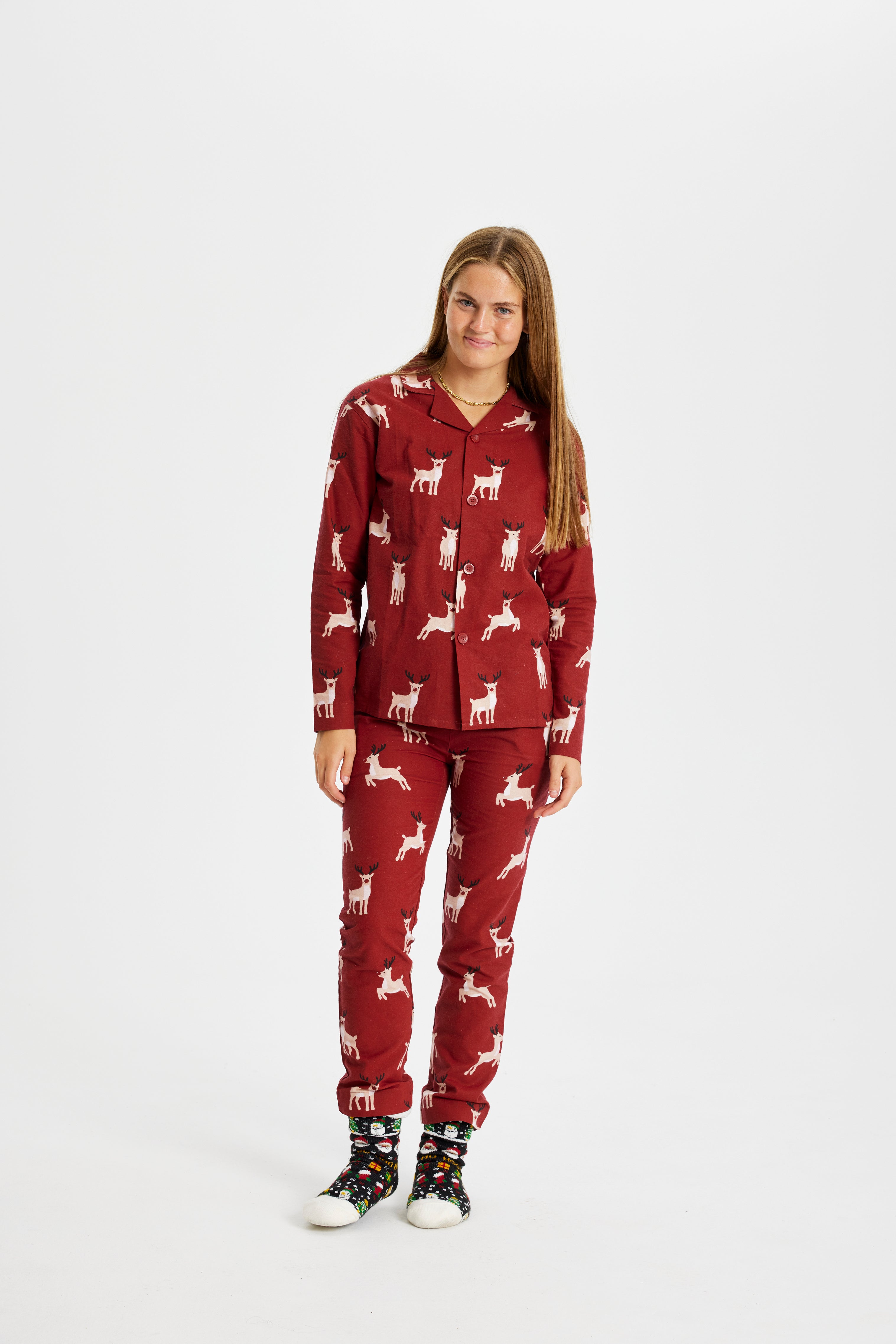 Een poserende vrouw in een rode kerstpyjama met rendieren erop.