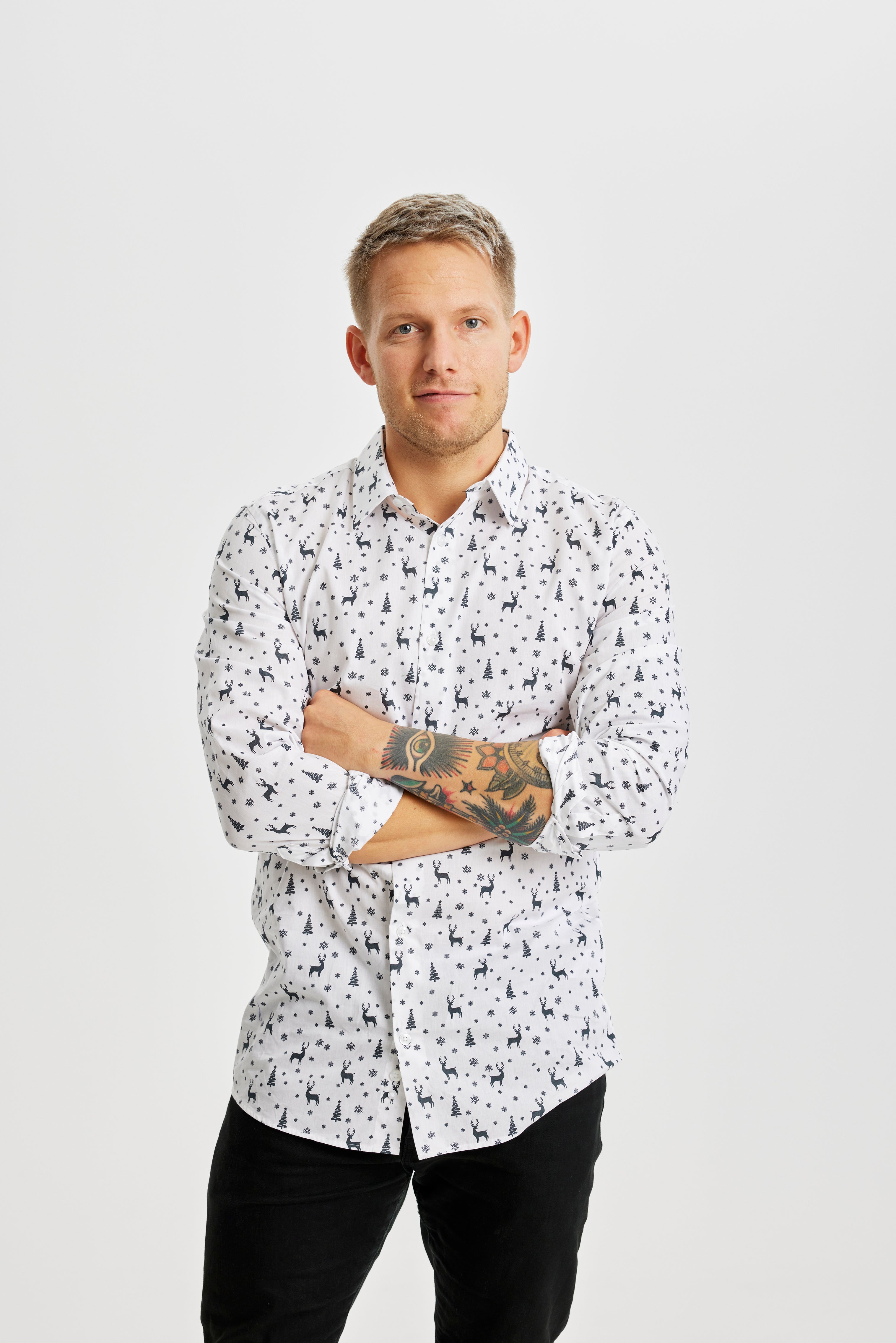 Een man in kleermakerszit die een wit kerstoverhemd draagt.