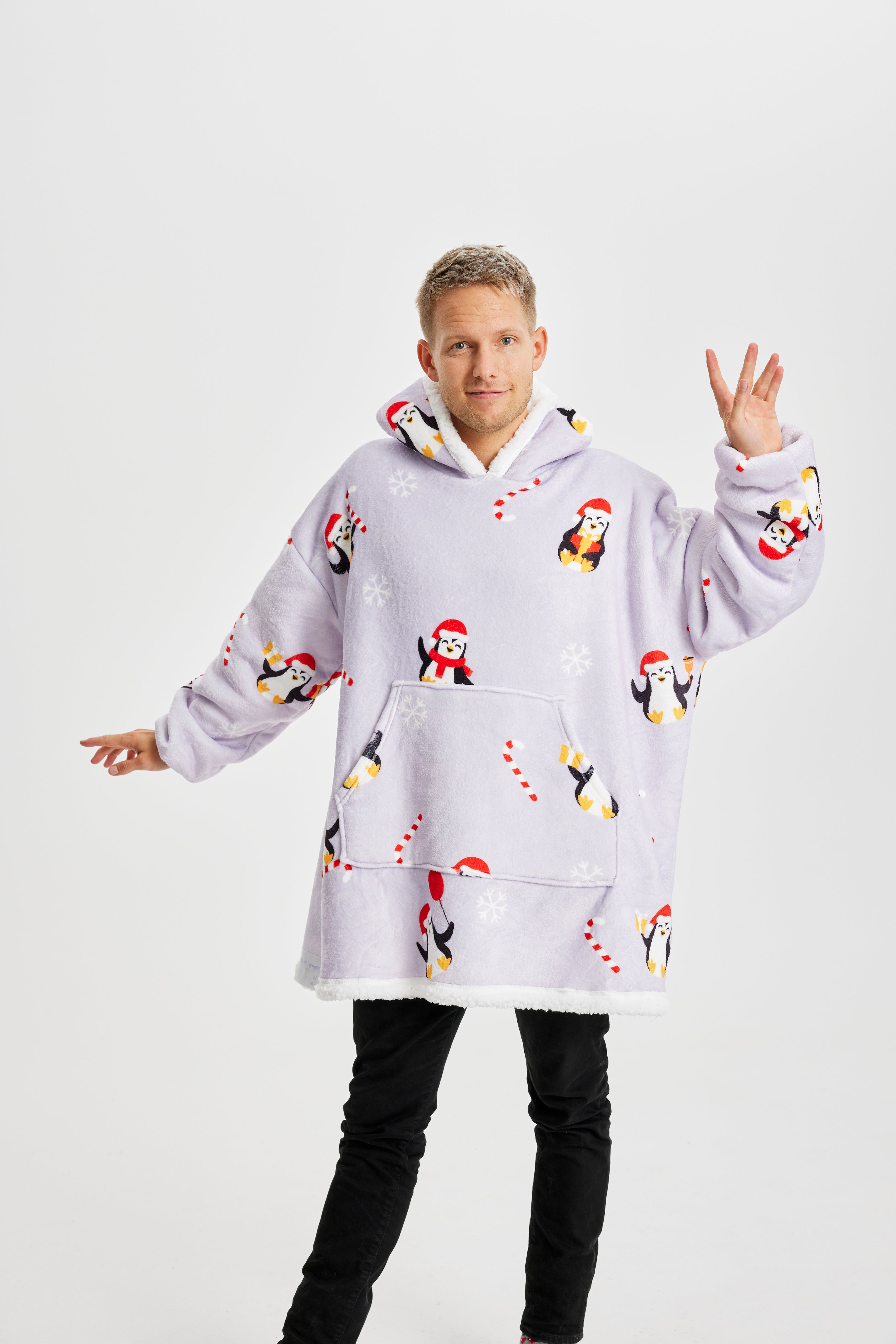 Een lachende man die een lichtpaarse kerst hoodie draagt met pinguïns erop.