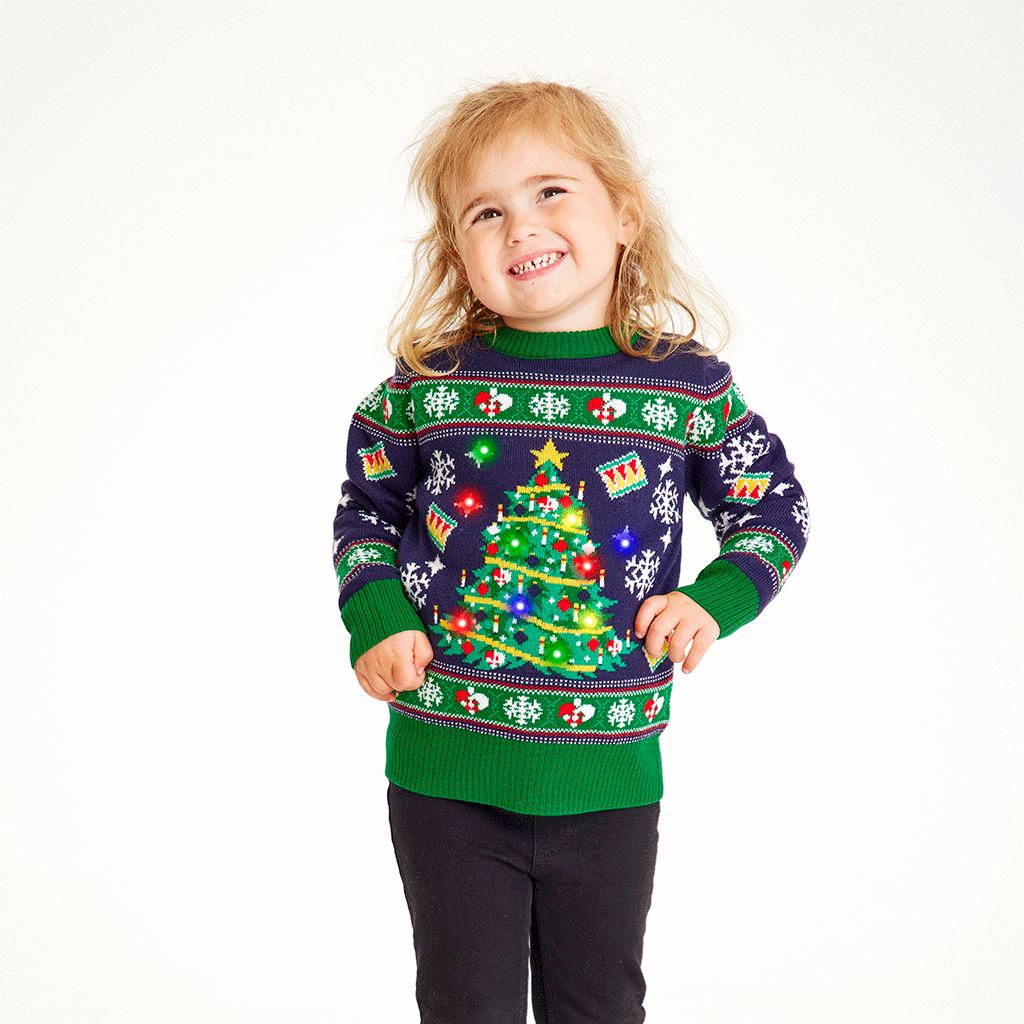 Een lachend kind in een blauwgroene outfit met een twinkelende kerstboom.