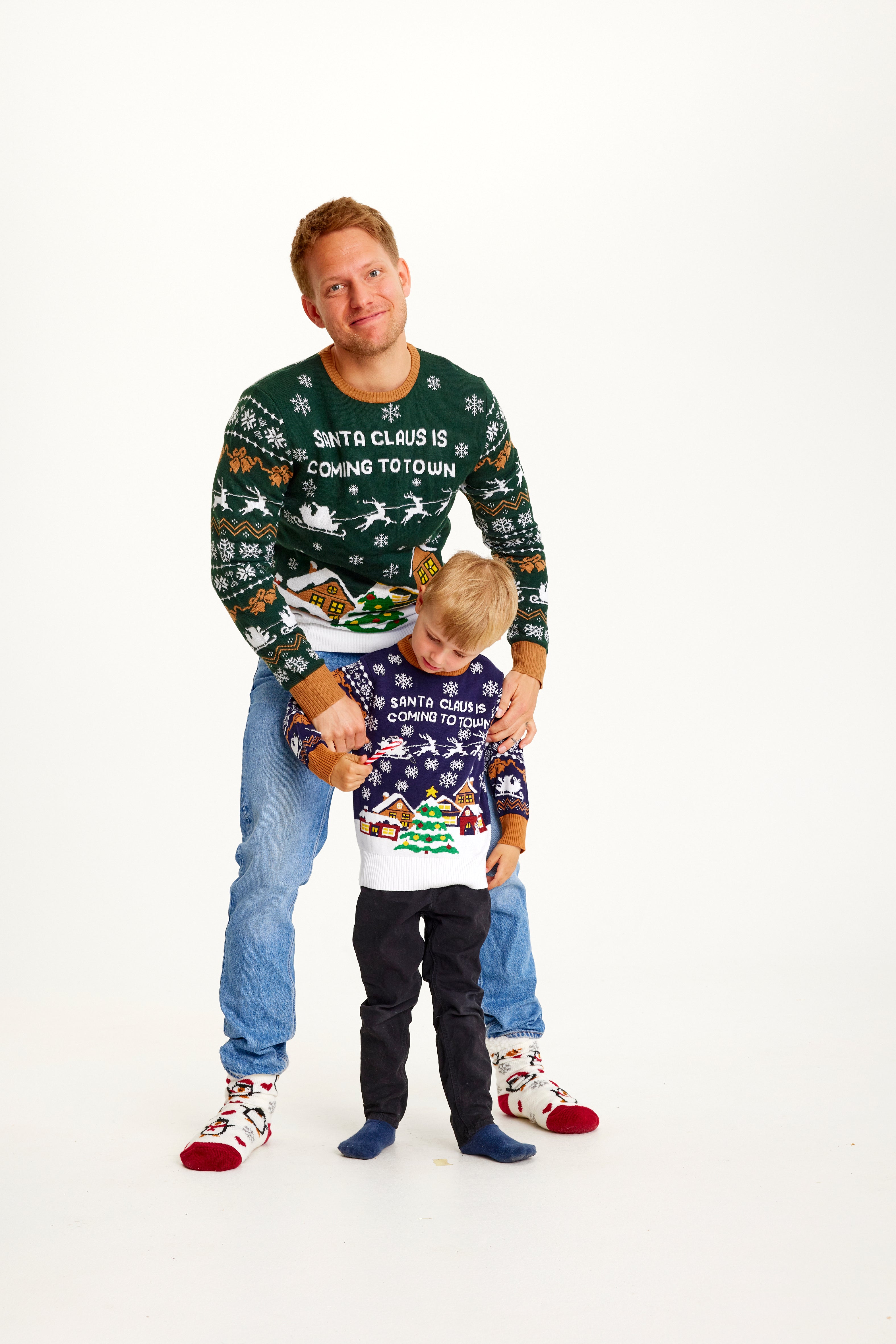 Een man en een kind die een kersttrui dragen met een besneeuwde stad.